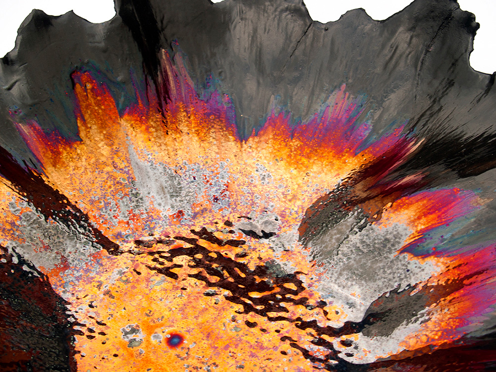 A dramatic macro close-up of dynamic luster glaze texture on a ceramic vessel by Alireza Rostami, showing vivid explosion of golden yellow, fiery orange, and iridescence purple hues meeting a jagged dark border.