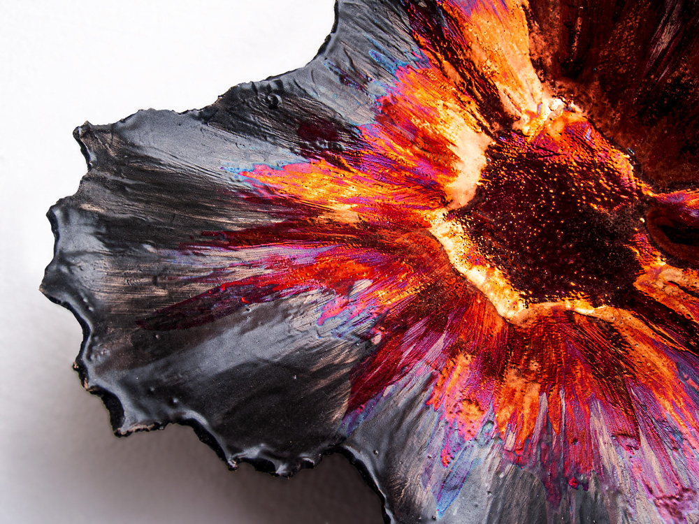 A high-resolution horizontal close-up of a ceramic sculpture by Alireza Rostami, featuring a radiant explosion of crimson, magenta, and gold metallic luster glazes flowing down to a dark matte tectonic rim.